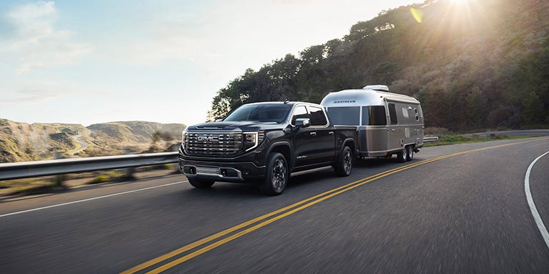 An All-New Black 2024 GMC Sierra 1500 pulling an Airstream trailer on a highway through the hills of Bloomer, WI.